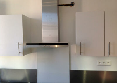 Mur de cuisine équipé d’une hotte inox, de meubles hauts et d’appareillages électriques neufs, dans un appartement entièrement remis à neuf