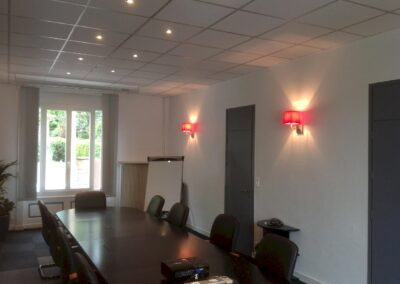 Vue latérale de la salle de réunion, montrant les spots au plafond et appliques murales rouges installés lors de la rénovation électrique